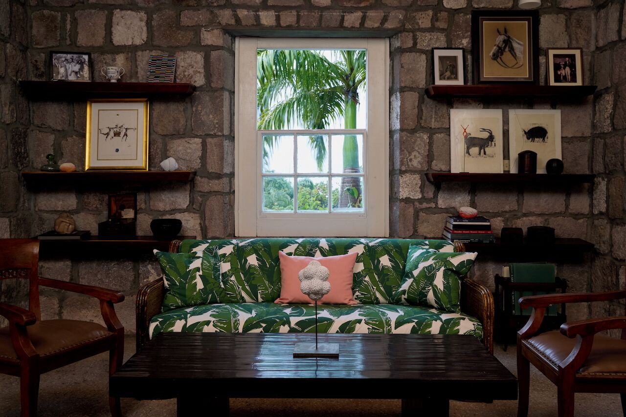 A cozy room with a stone wall, a window with a view of greenery, a green patterned sofa, and wooden furniture.