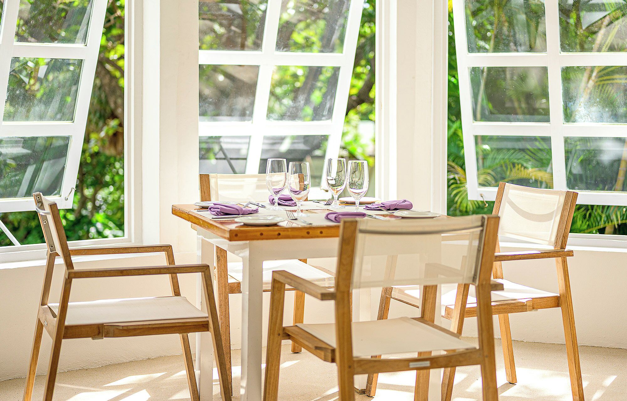 Un comedor con mesa y sillas de madera, ventanas amplias con vistas a zonas verdes y un cuadro en la pared.
