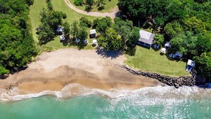 Vista aérea de un complejo turístico en la playa, con una playa de arena, aguas turquesas cristalinas y varias cabañas rodeadas de exuberante vegetación.