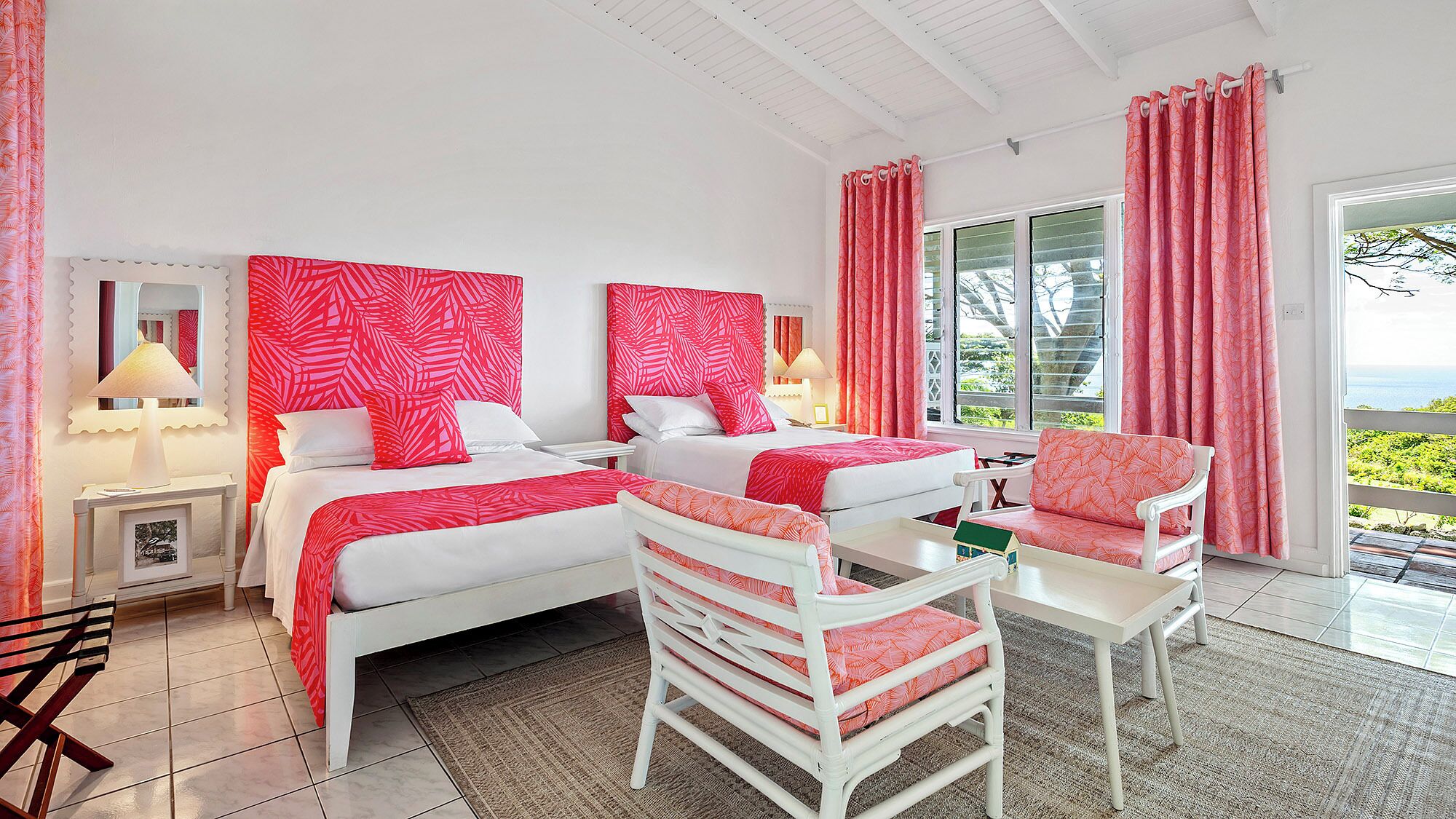 Une chambre d’hôtel avec deux lits, une chaise, une table et vue sur l’océan.