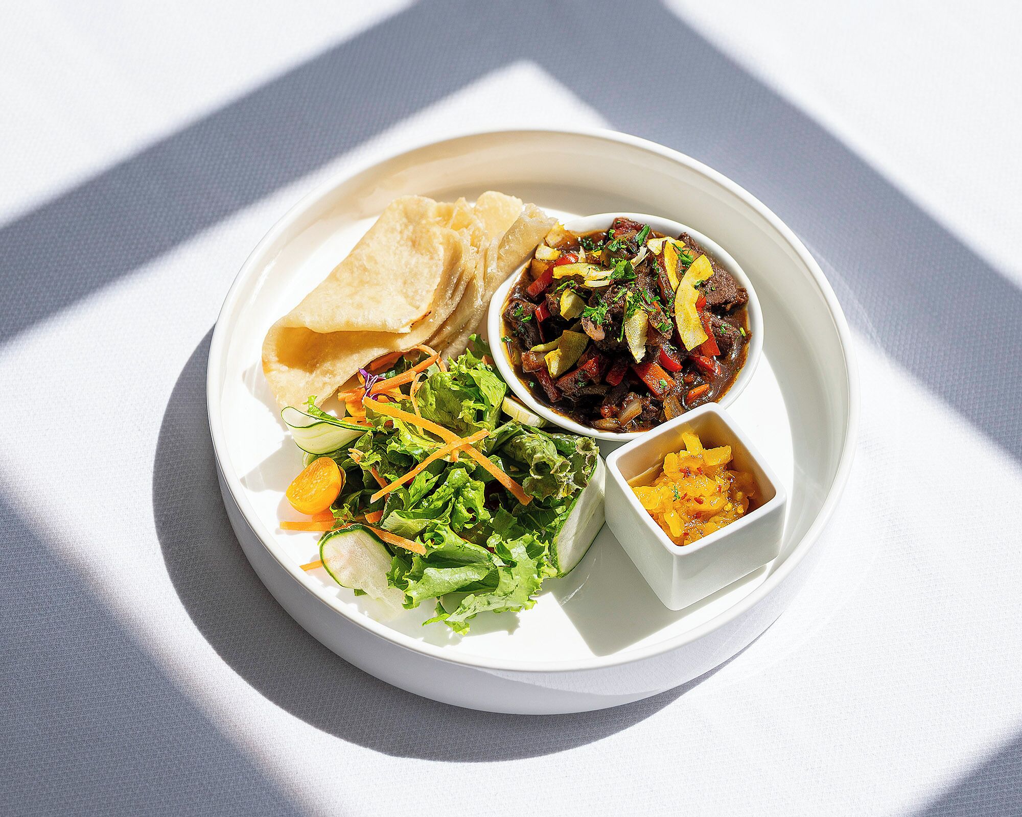 A plate with a variety of foods including a salad, a bowl of stew, and a small dish of what appears to be a fruit compote.