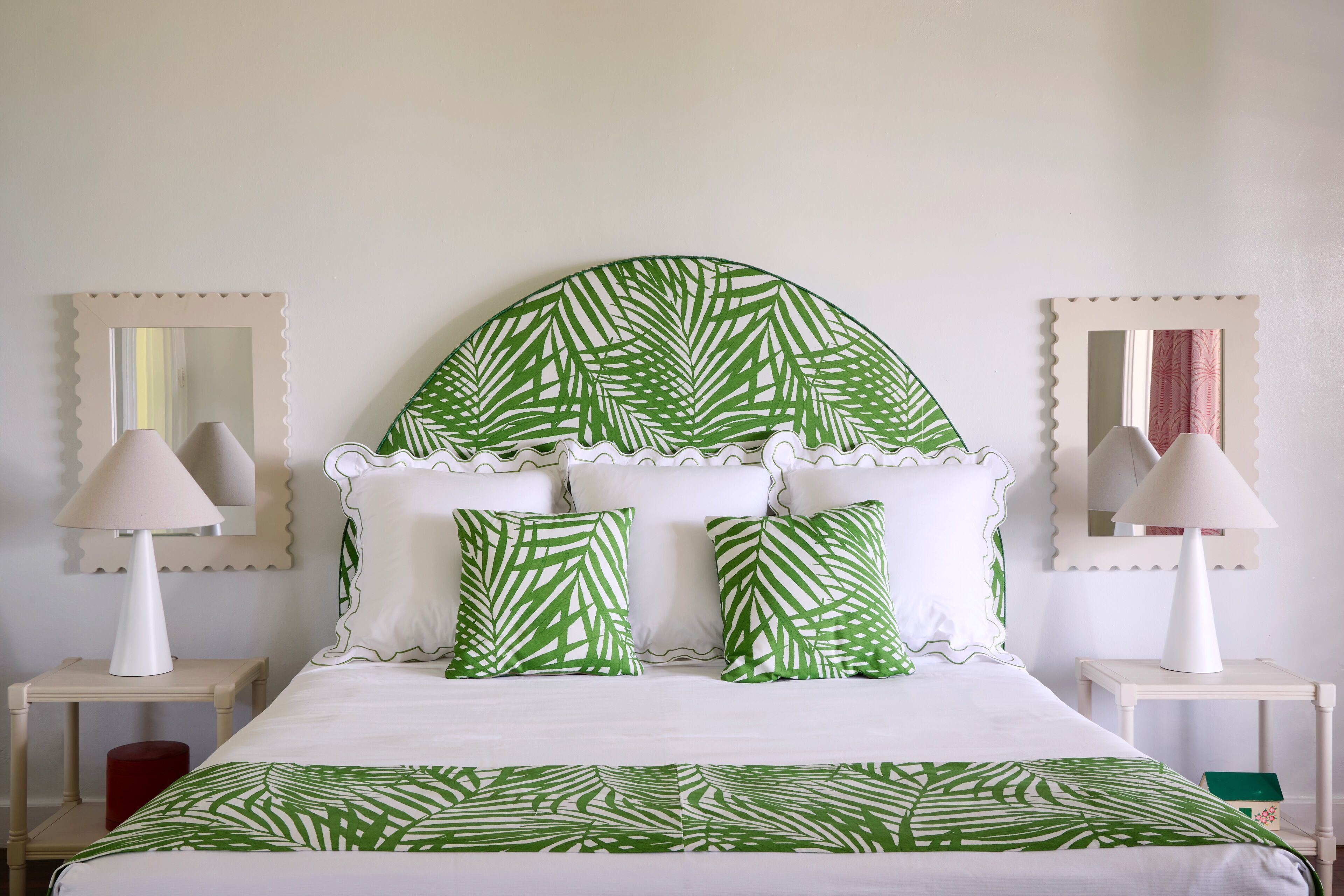 A bed with a leaf-patterned headboard, white bedding, and two bedside lamps.
