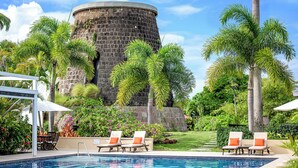 Un área de piscina con sillas de descanso, una estructura de piedra y vegetación tropical.