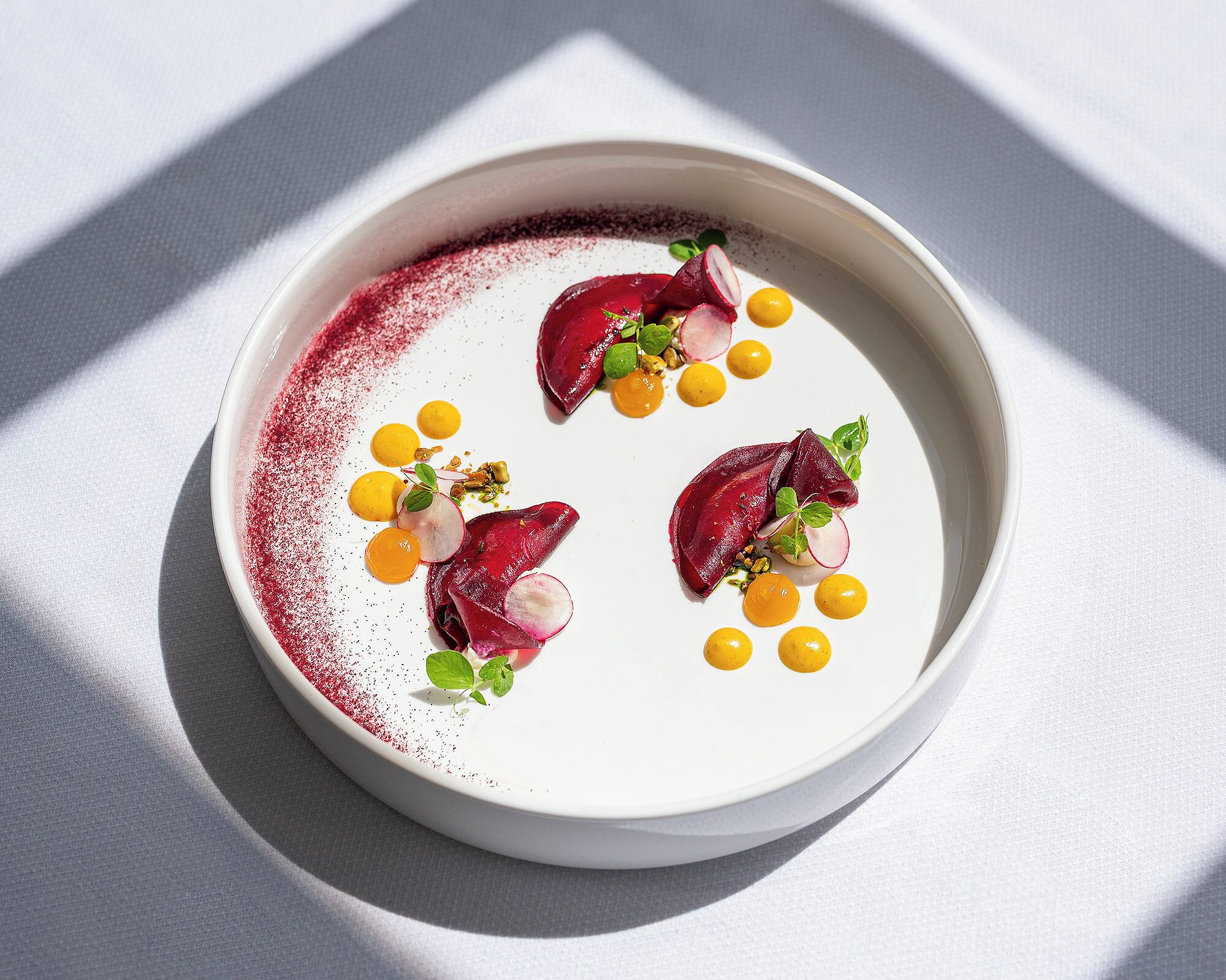 Un plato blanco con un postre que incluye rodajas de remolacha, esferas amarillas y hojas de menta.