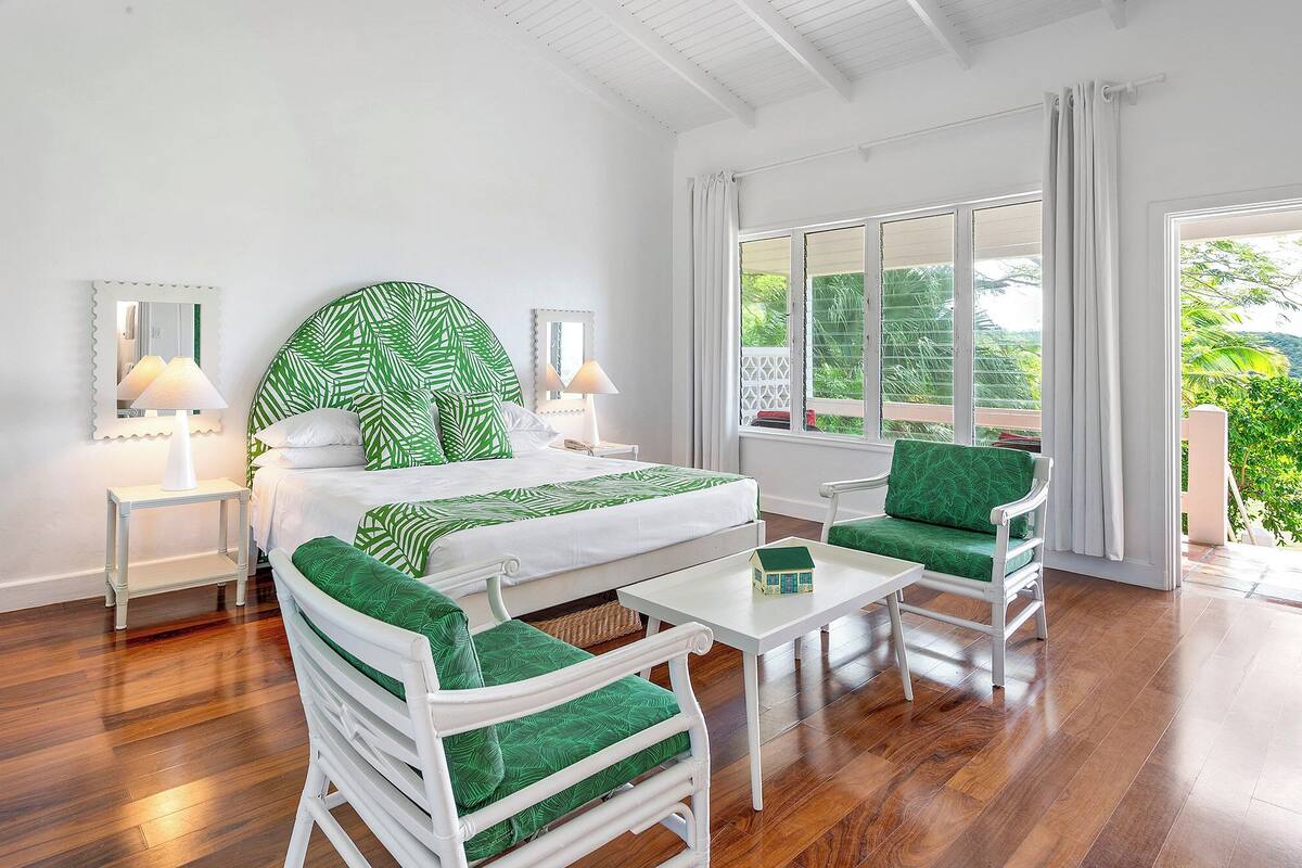 A room with a bed, two nightstands, a table, two chairs, and a window with curtains.