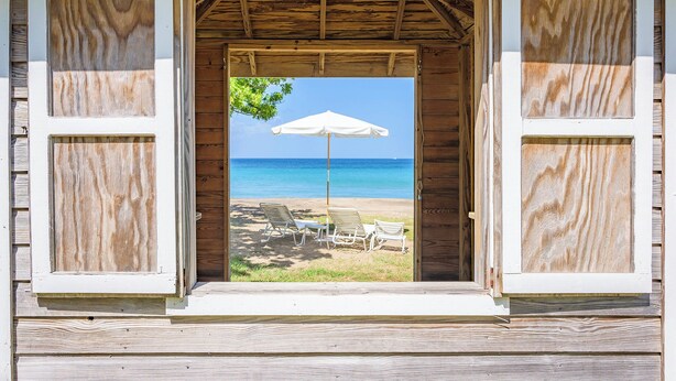 Puerta de madera con vista a una playa y un paraguas.