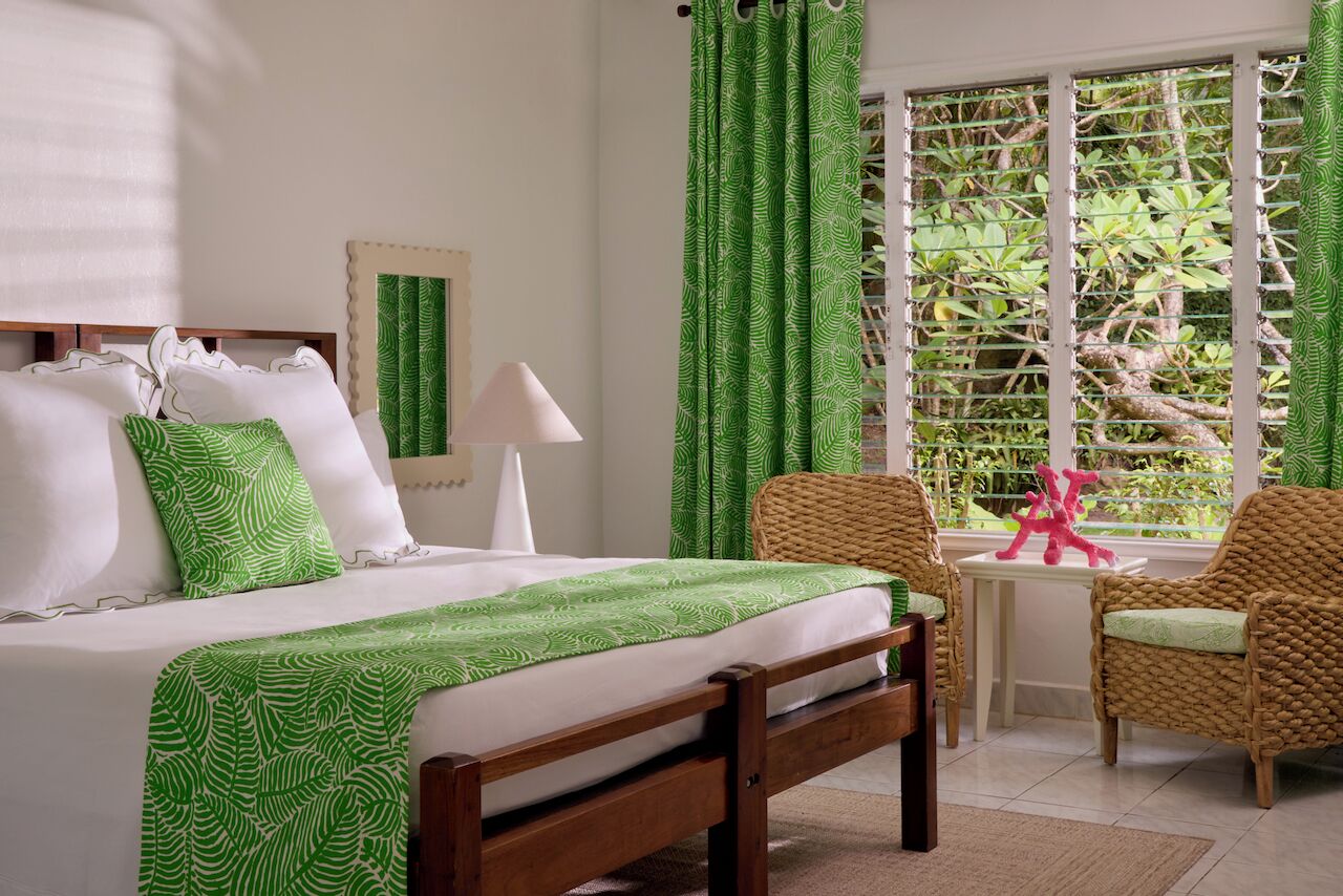 Una camera da letto ordinata con un letto, una lampada da comodino e vista su del verde attraverso una finestra con inferriate metalliche.