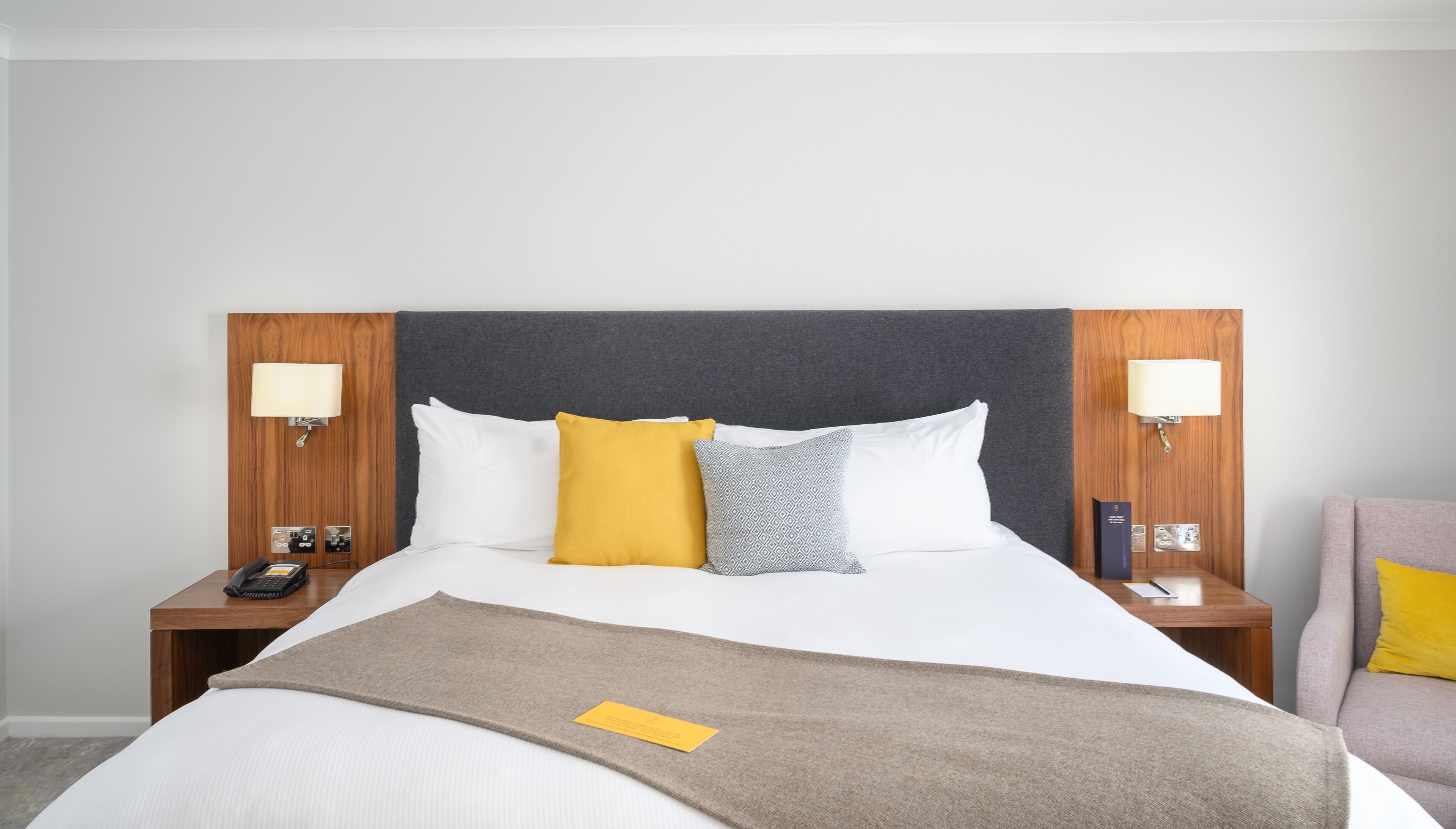 A hotel room with a large bed, two bedside tables with lamps, a telephone, and a chair.