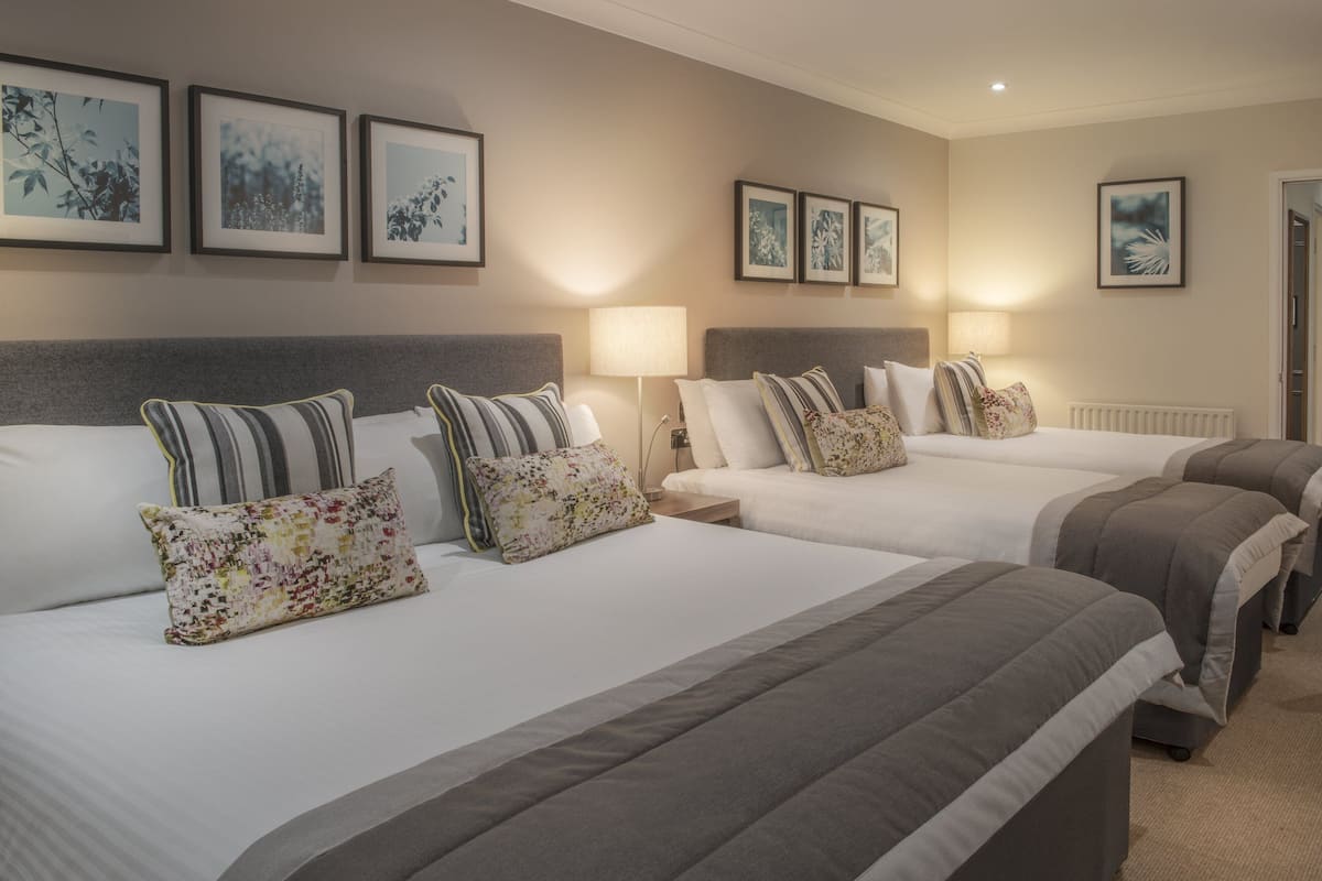 A hotel room with three beds, each with a different pillow design. There are wall-mounted picture frames and a radiator.