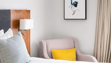 A hotel room with a bed, a chair, a lamp, a framed picture, and a curtain.