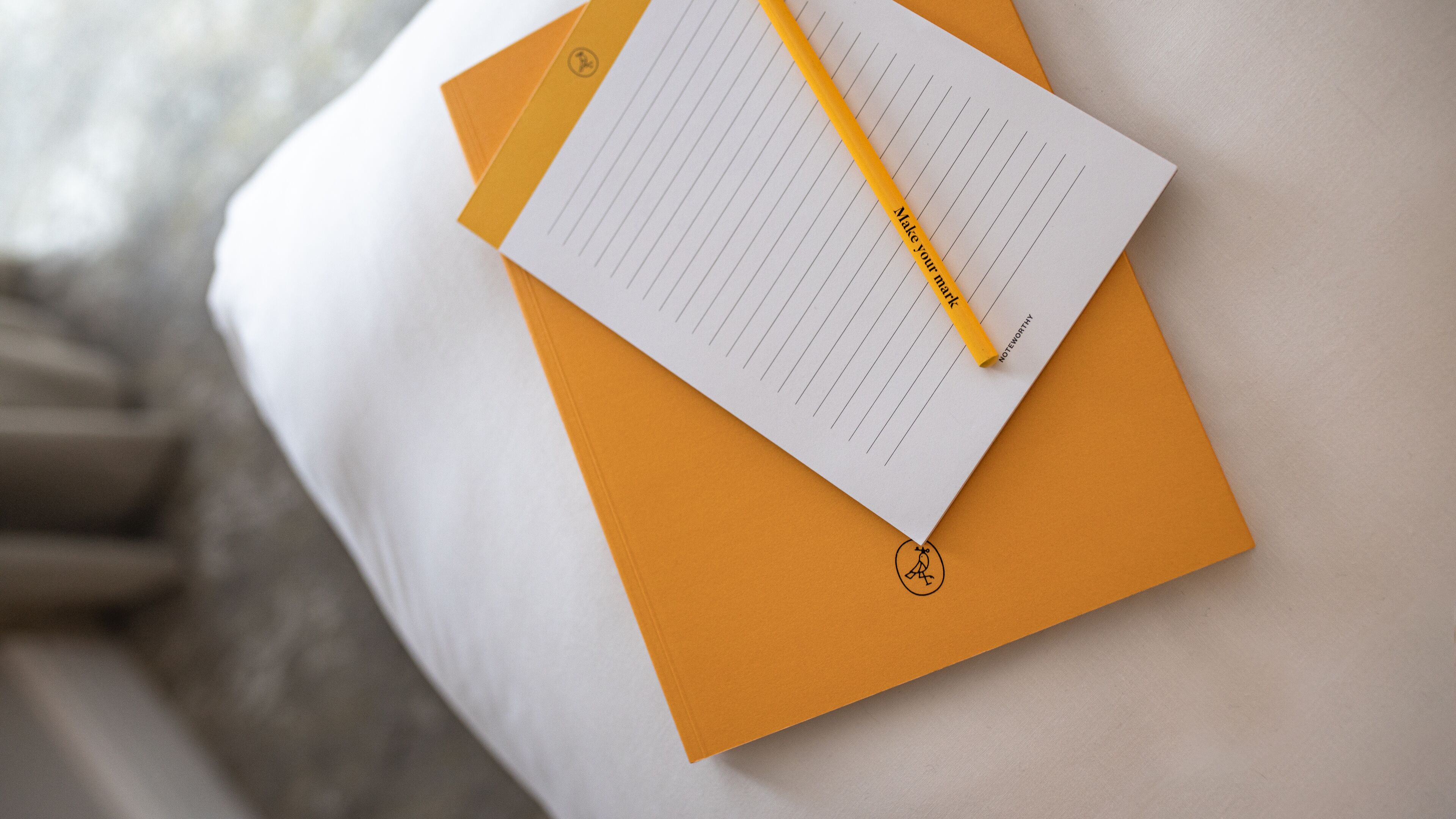 A notebook with a yellow pencil on top of an orange folder.