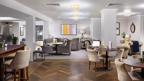 A hotel lobby with a wooden herringbone floor, a seating area with sofas and chairs, a dining table, and a large abstract painting on the wall. - voco Oxford Spires by IHG (Oxford)