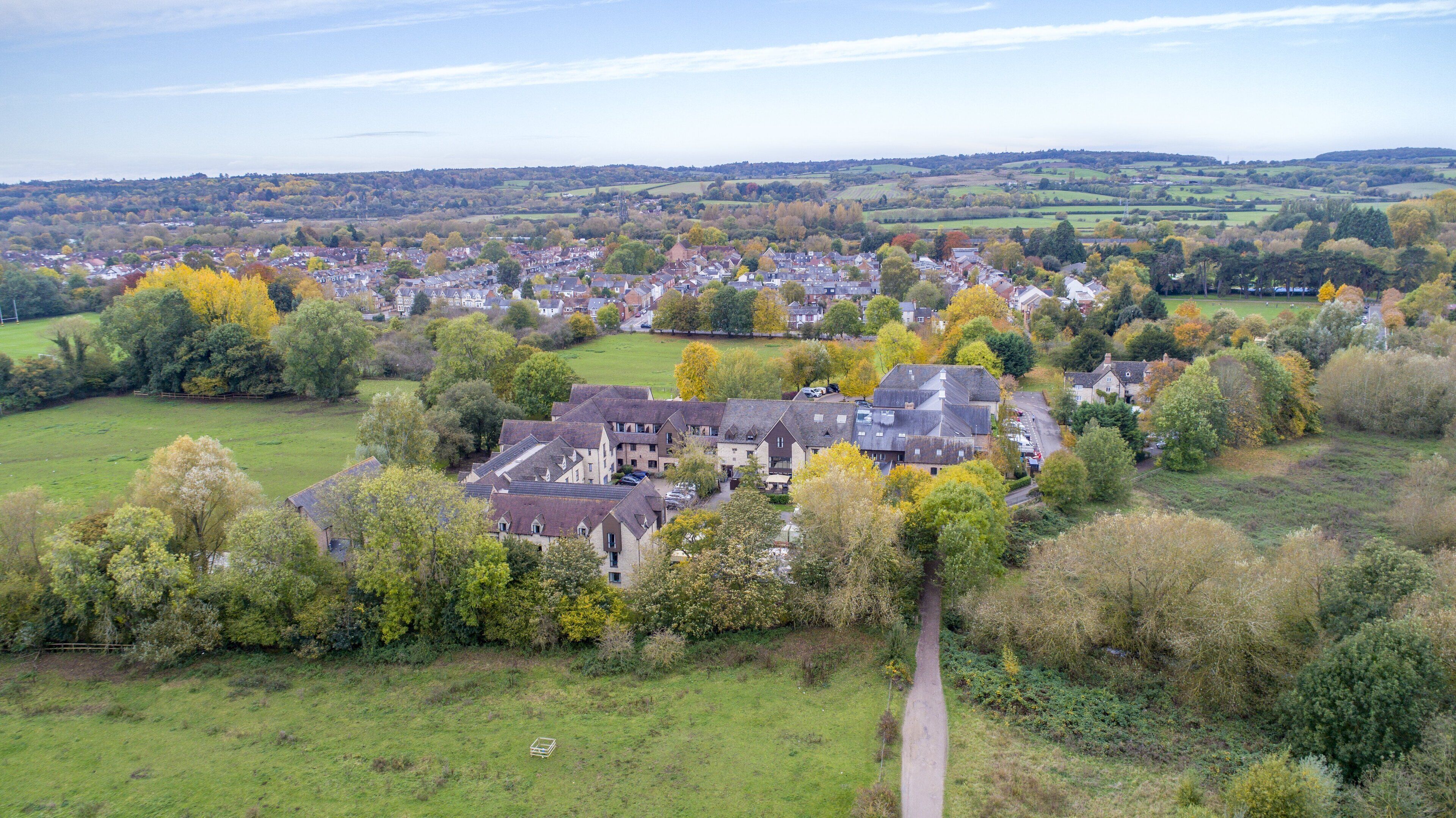 An aerial view of a residential area with houses, a large building with multiple stories, and surrounding greenery.