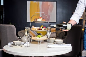 A three-tiered dessert stand with various pastries and fruits, a bottle of wine being poured into a glass, and a table setting with cups and a teapot. - voco Oxford Spires by IHG (Oxford)
