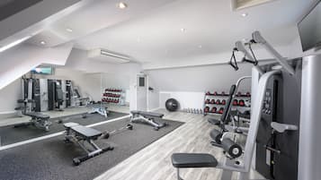 Un gimnasio moderno con equipo de ejercicio diverso, un muro con espejos y un zapatero con varios pares de zapatos.