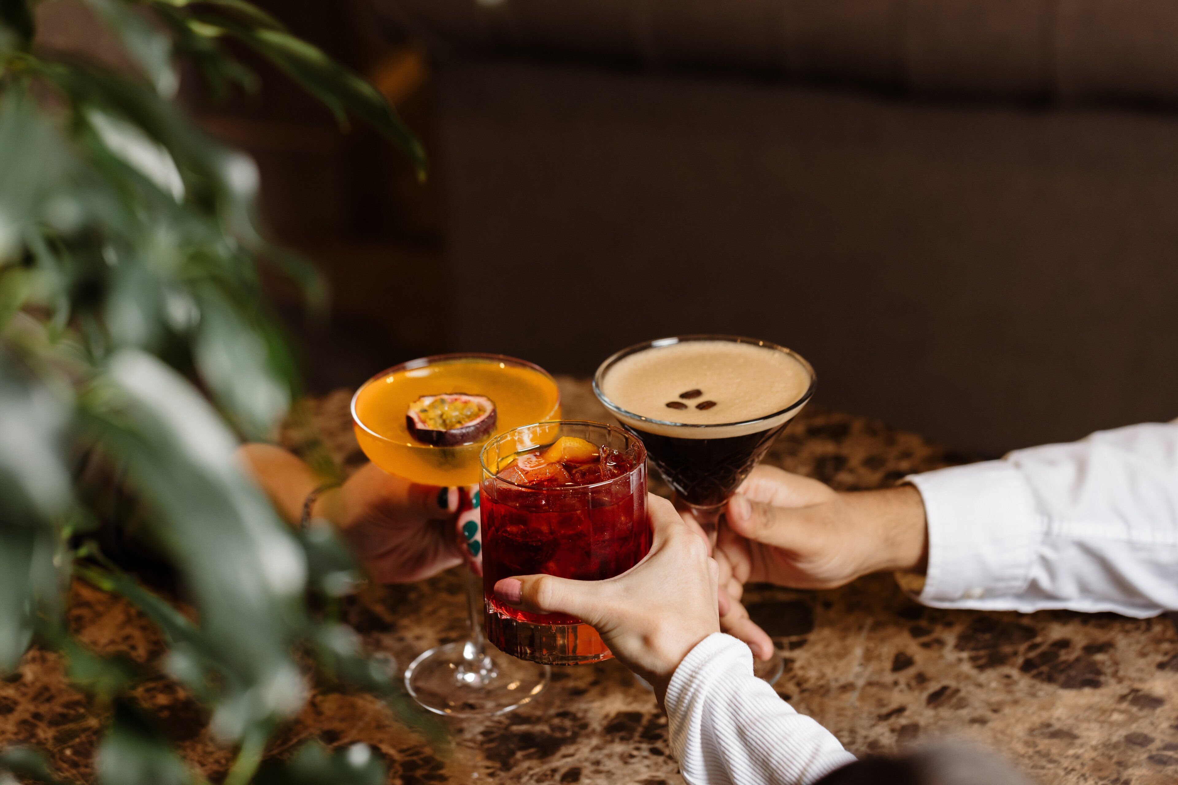 A close-up of three drinks on a table, with hands holding them.