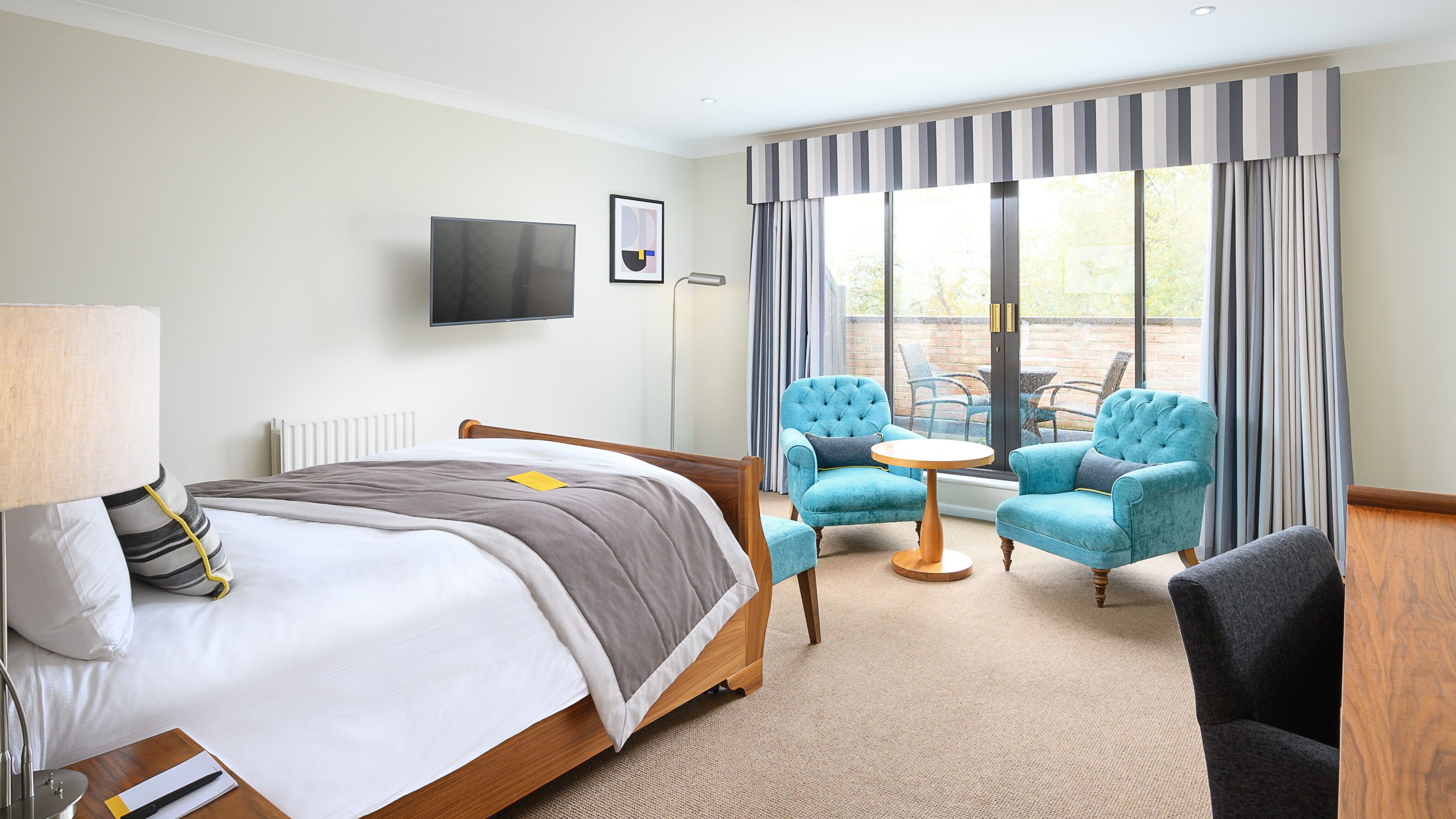 Ein Hotelzimmer mit Bett, Schreibtisch, Stuhl, Fernseher und Blick ins Freie.