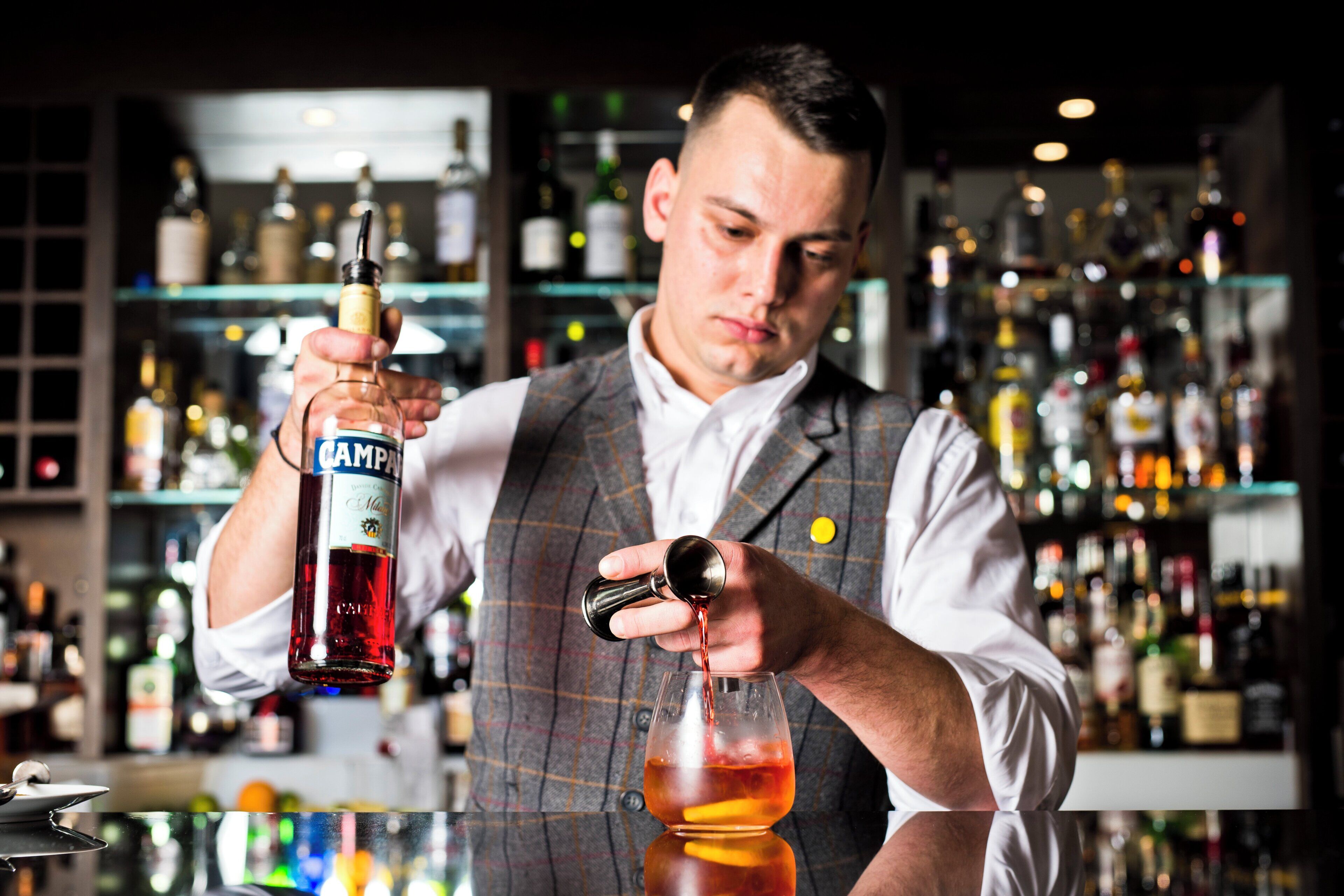 A bartender pouring a drink from a bottle labeled 'Campania' into a glass.