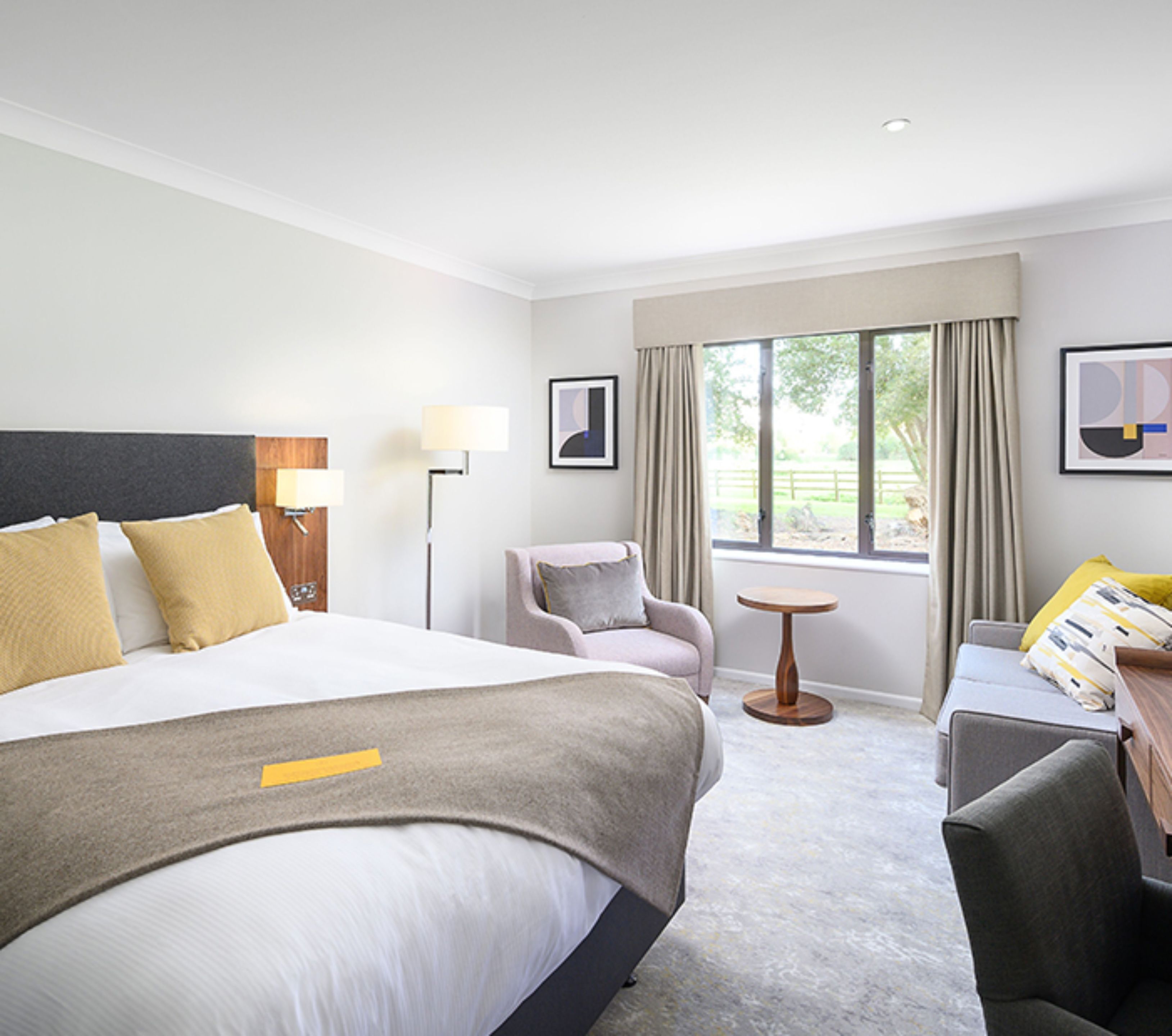 Ein Hotelzimmer mit einem großen Bett, einem Schreibtisch, einem Stuhl und einem Fenster mit Vorhängen.