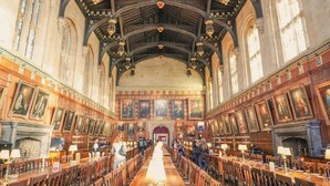 A long, narrow hall with wooden benches and tables, high ceilings with intricate woodwork, and large windows.