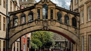 A stone bridge with arched design and stained glass windows, connecting two buildings. - voco Oxford Spires by IHG (Oxford)