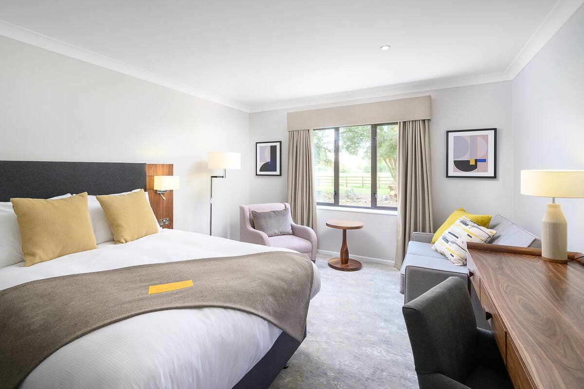 A hotel room with a large bed, a desk, a chair, and a window with curtains.
