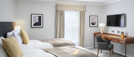 Habitación de hotel con cama, escritorio, silla, televisor y dos cuadros en la pared.