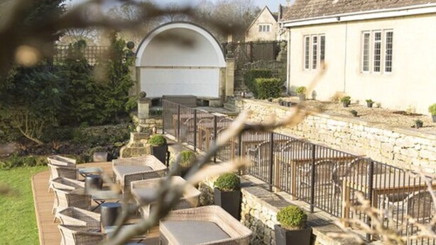 An outdoor patio with wicker furniture and a stone wall. - The Painswick (Stroud)