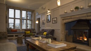 A cozy living room with a fireplace, seating area, and large windows. - The Painswick (Stroud)