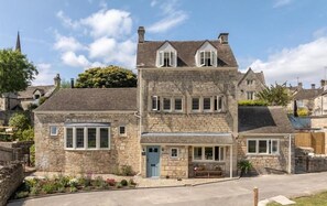 A stone building with a central entrance, a small porch, and a garden area with flowers.