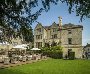 A large stone building with a courtyard, outdoor seating, and a well-maintained lawn.