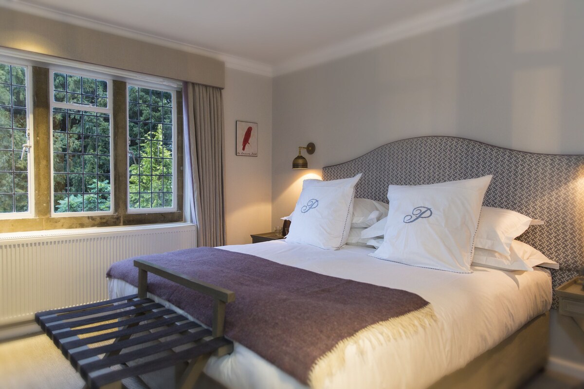 A neatly made bed with a headboard, a bedside table with a lamp, and a window with curtains.