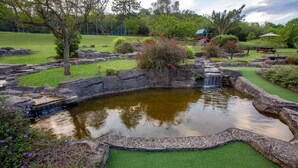 A miniature golf course with a pond, green artificial grass, and various plants. - Pine Lake Inn (Mbombela)
