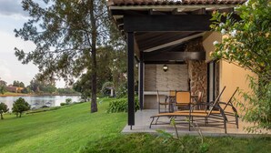 A covered patio with outdoor furniture, a stone fireplace, and a view of a lake. - Pine Lake Inn (Mbombela)