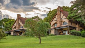 A large, two-story house with a stone chimney, a covered patio, and a well-maintained lawn. - Pine Lake Inn (Mbombela)