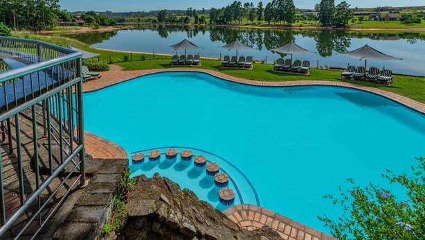 A swimming pool with a view of a lake, lounge chairs, and a stone staircase. - Pine Lake Inn (Mbombela)