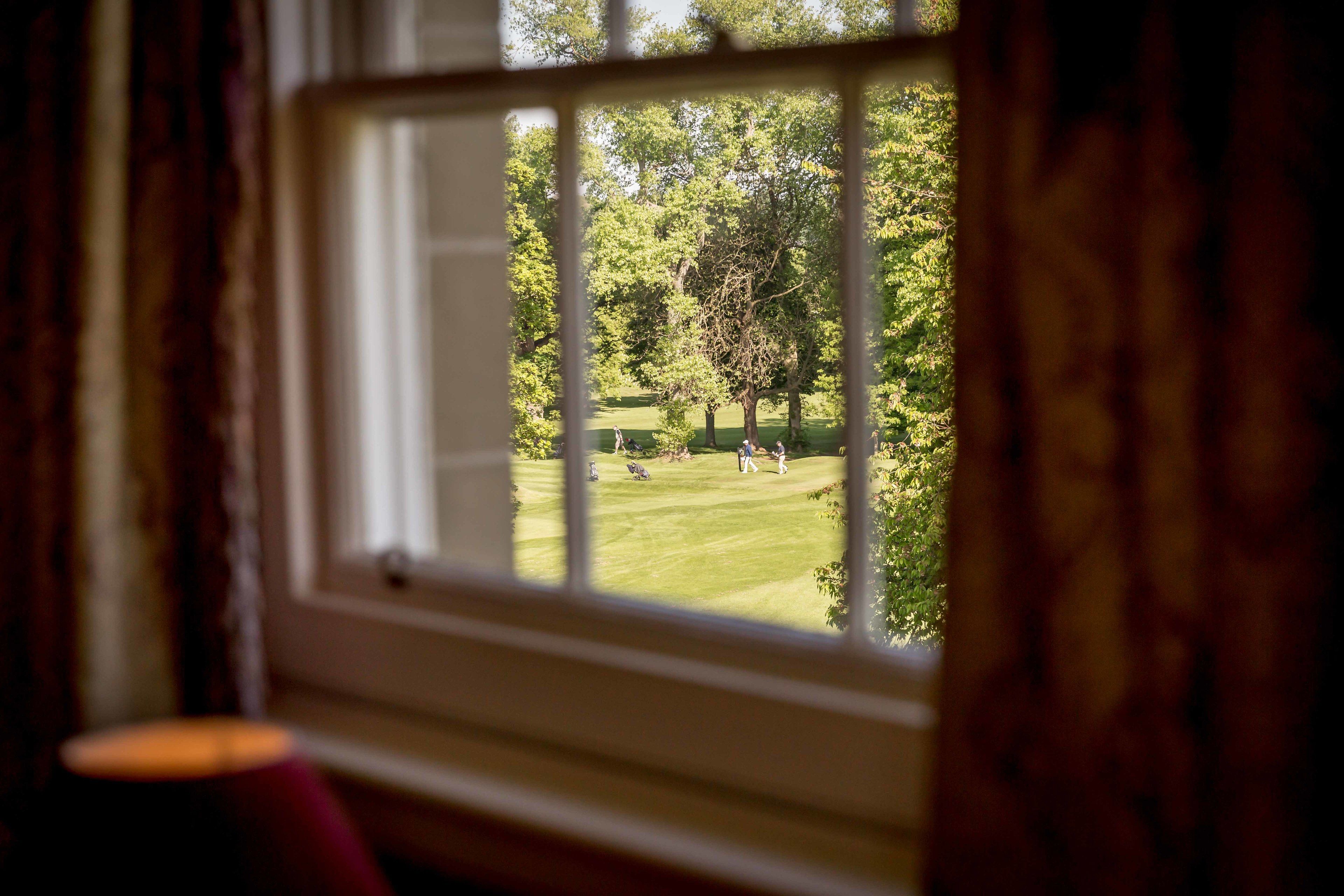 Una ventana con vistas a un césped verde y árboles.
