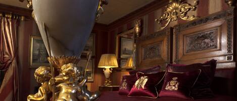 A luxurious bedroom with a large bed, ornate gold fixtures, and framed artwork on the walls.