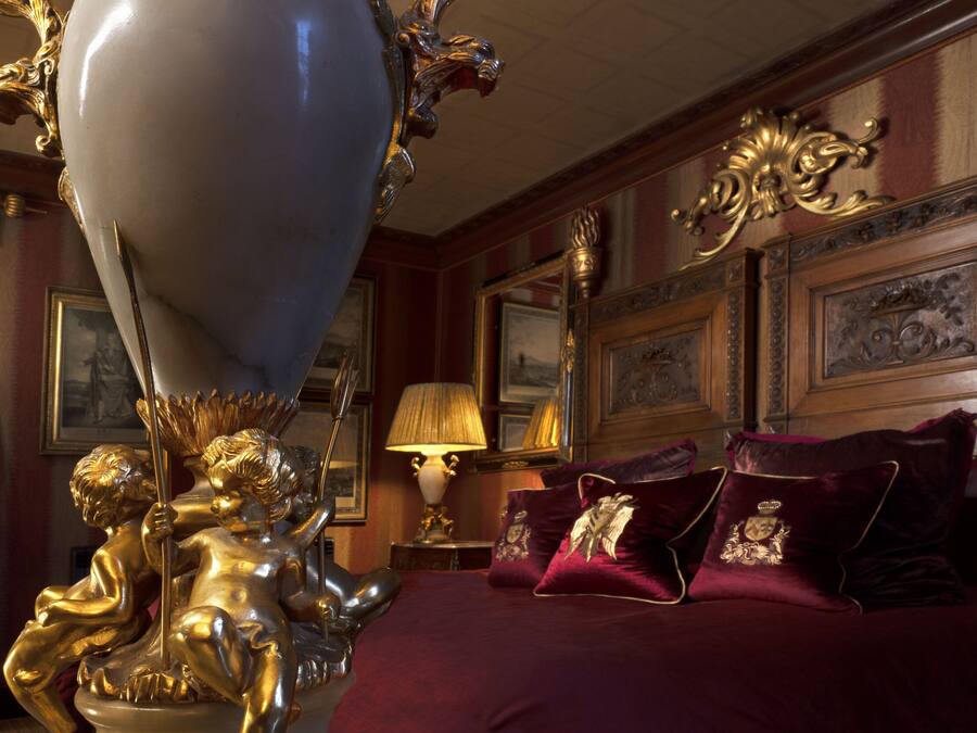 A luxurious bedroom with a large bed, ornate gold fixtures, and framed artwork on the walls.