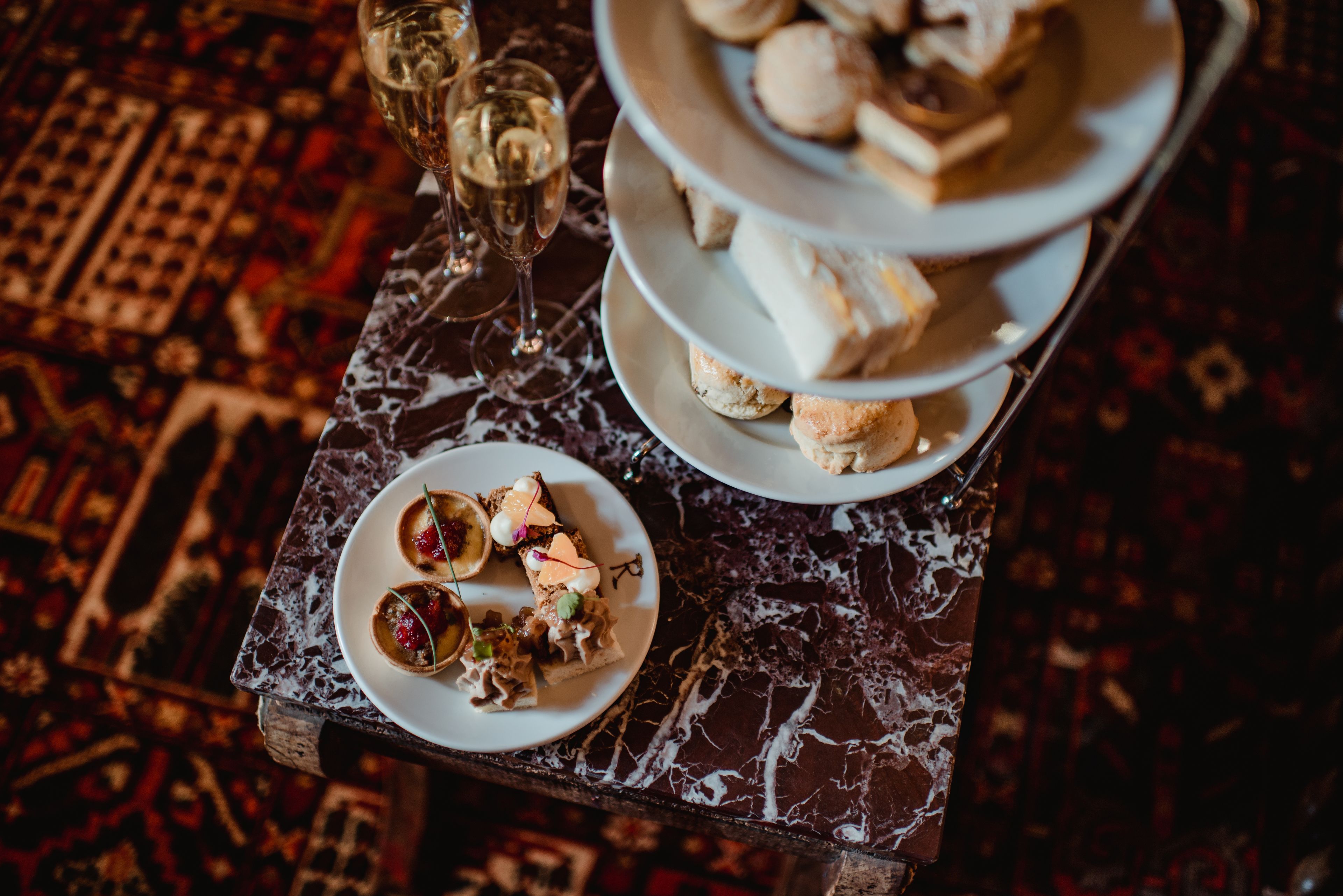A marble table with a tiered dessert stand and a plate of appetizers.