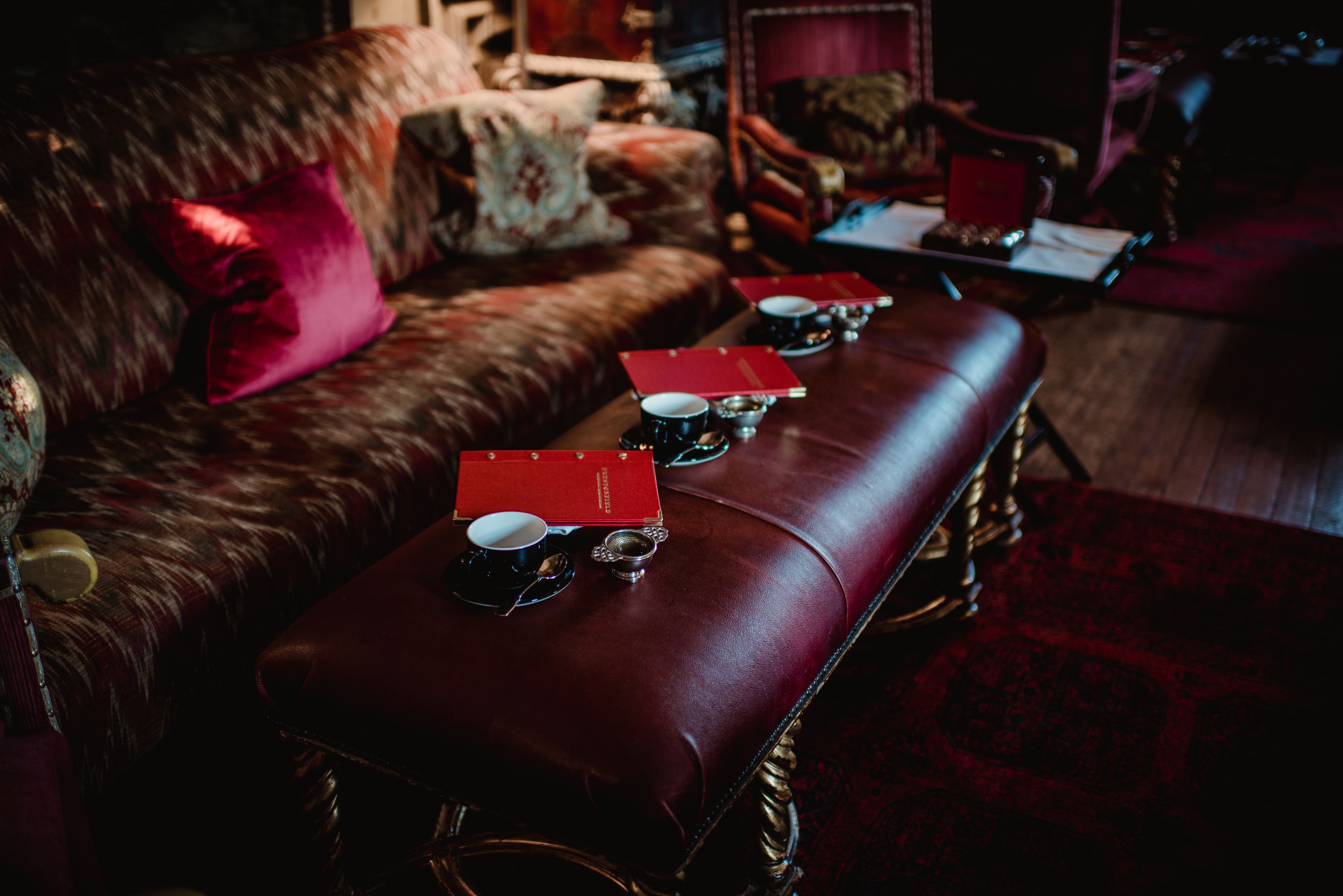 A leather sofa with a red cushion, a red tray table with three cups and saucers, and a red book.