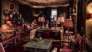 Una habitación ricamente decorada con muebles ornamentales, incluyendo un conjunto de sofás, sillones y una mesa de centro, con un espejo grande y lámparas decorativas.