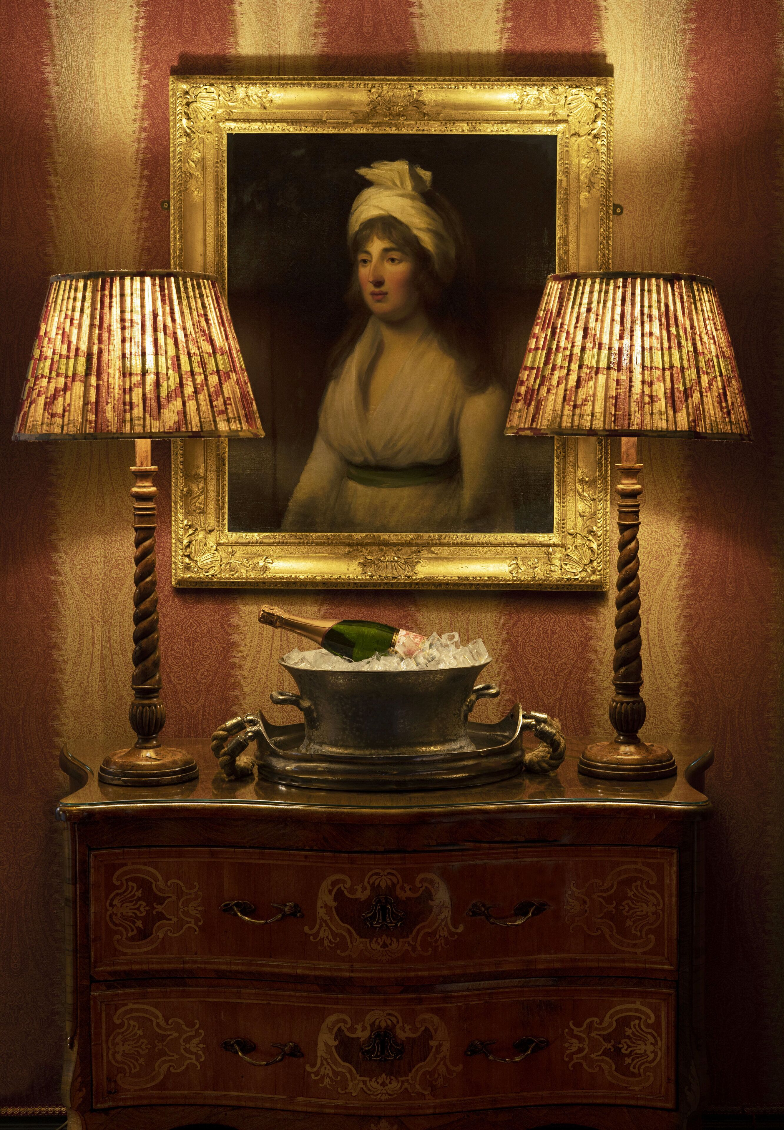 Una habitación de estilo vintage con un aparador de madera, dos lámparas y un retrato enmarcado en la pared.