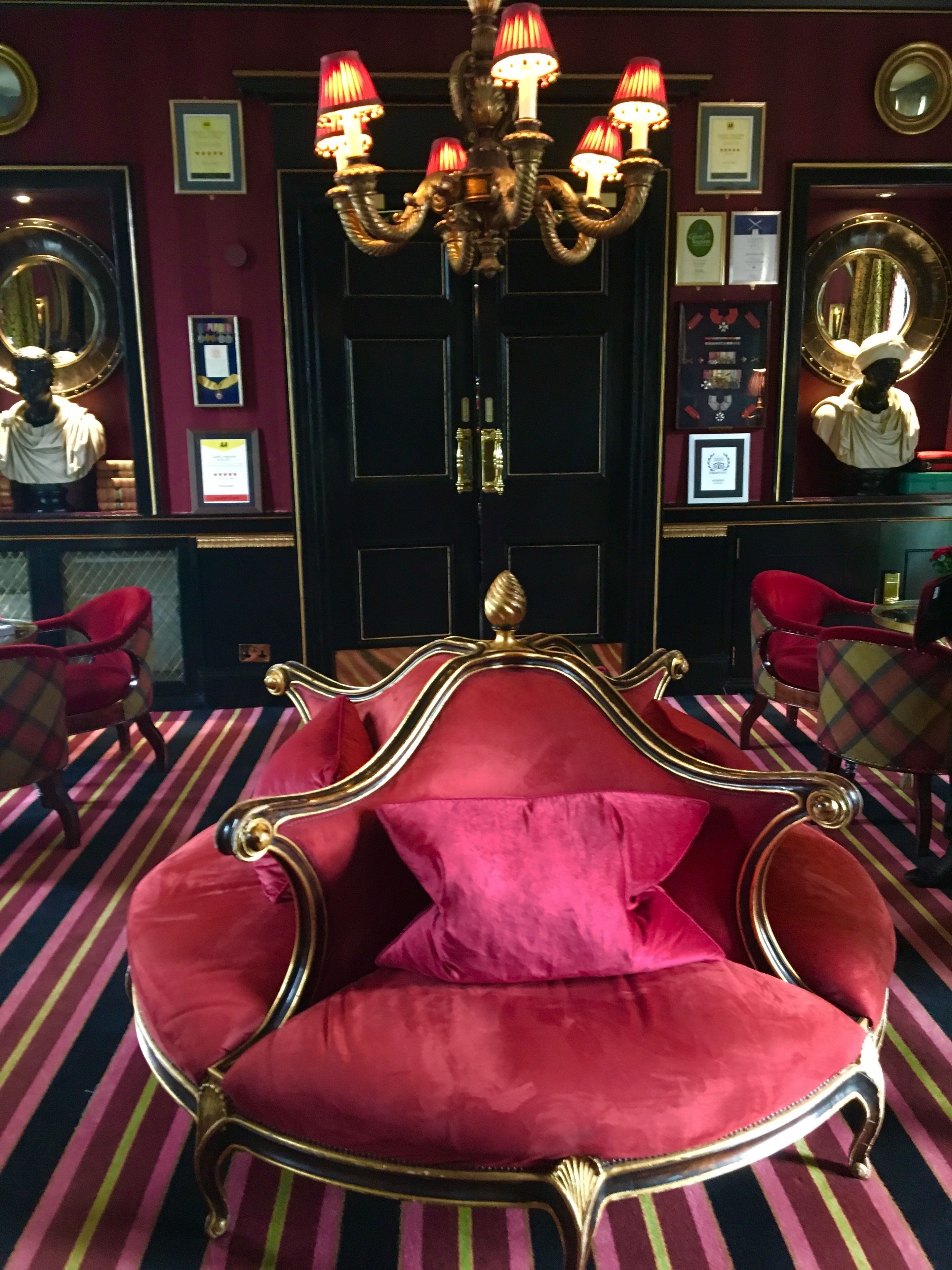 A room with a red velvet chair, a chandelier, and a black door with framed certificates.
