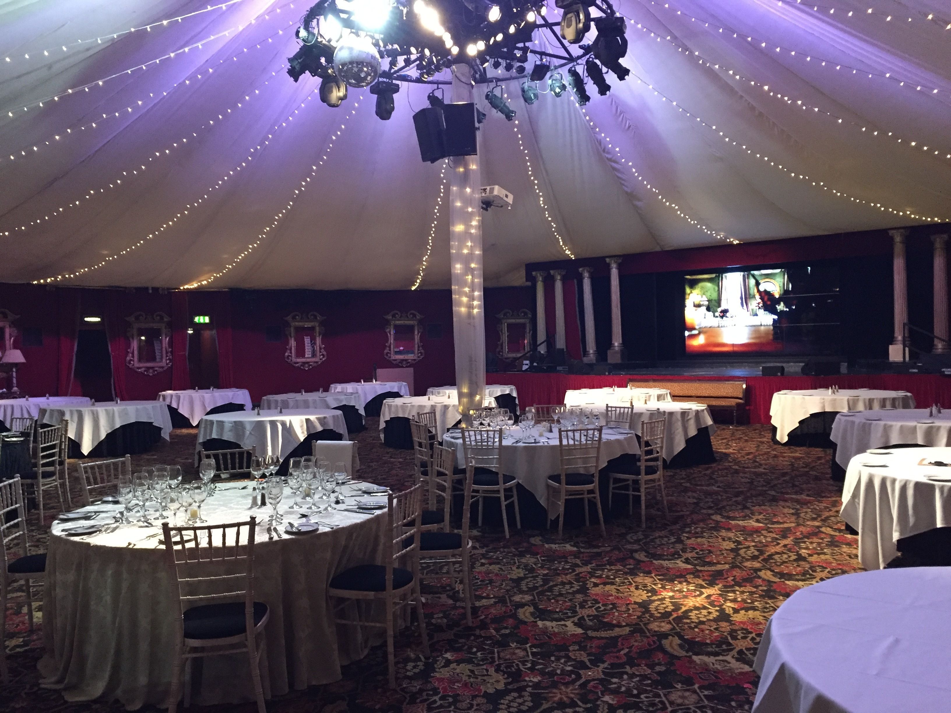 A banquet hall with round tables, white tablecloths, and chairs.