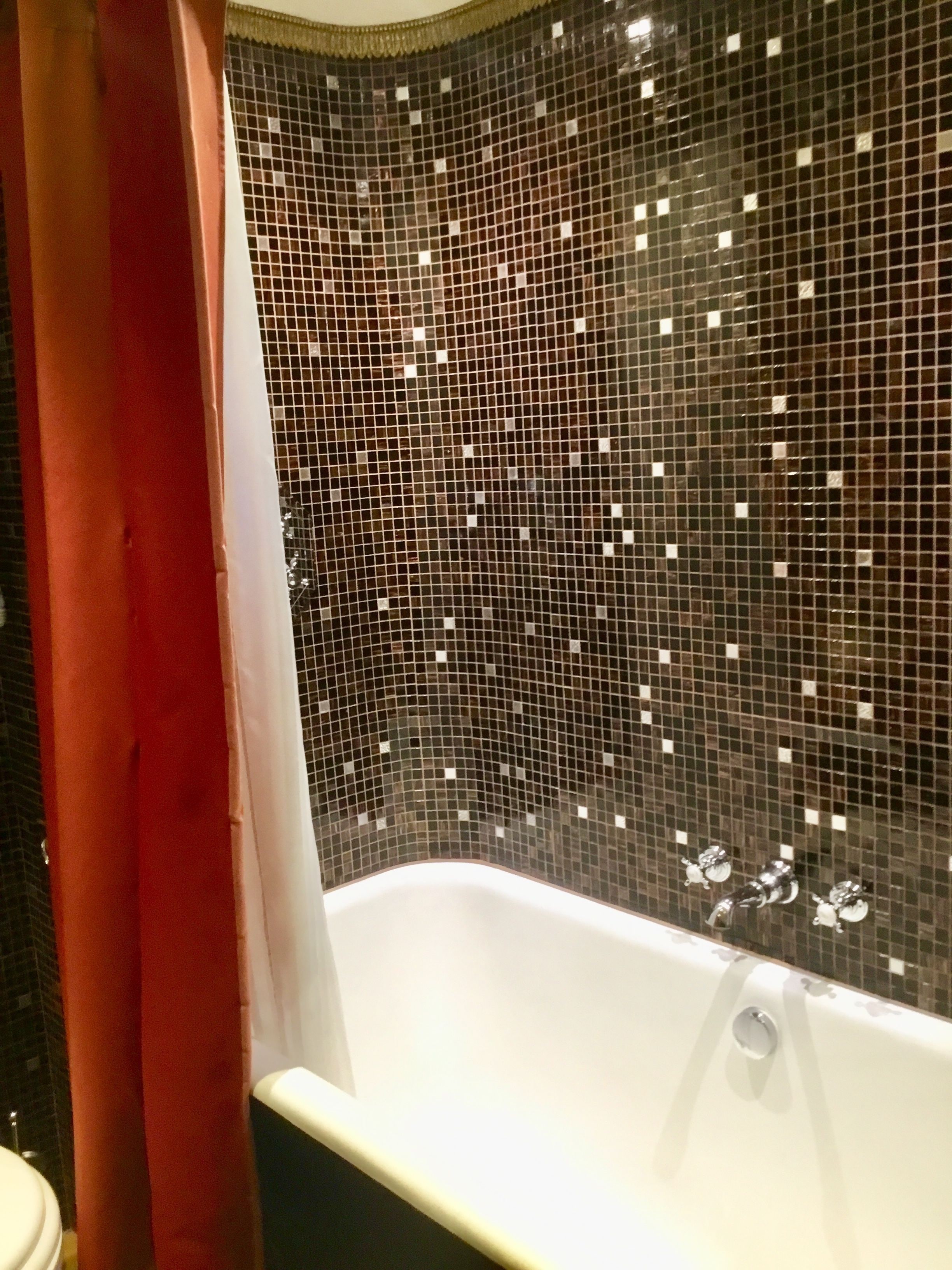 A bathroom with a bathtub, a shower curtain, and a tiled wall.
