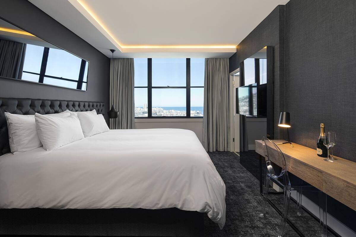 Una habitació d'hotel moderna amb un llit gran, un escriptori de fusta, una televisió i vista a la ciutat.