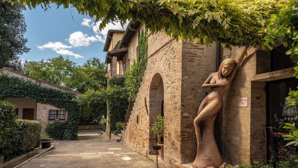 A courtyard with a statue, stone walls, and a reception sign. - Relais Della Rovere (Colle di Val d'Elsa)