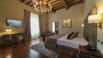 Una camera d'albergo con soffitto in legno, un letto con coperta, una scrivania con lampada, una sedia, una televisione e una finestra con tende.