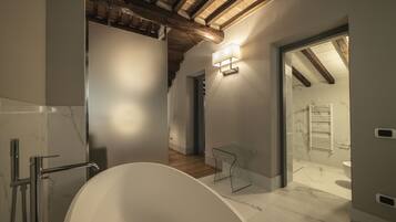 Un baño moderno con una bañera independiente, cabina de ducha de vidrio y una escalera visible que conduce a otra habitación.